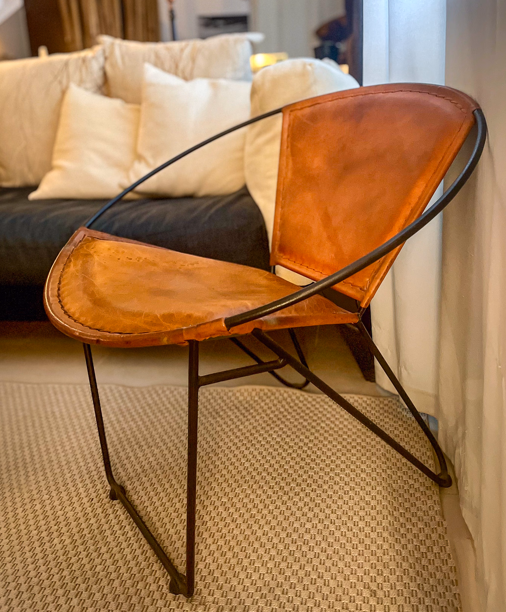 A cognac leather chair with a curved black metal frame, styled against cream cushions and a dark sofa